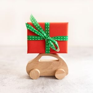A wooden toy car carrying a Christmas gift box wrapped in red with a green ribbon.